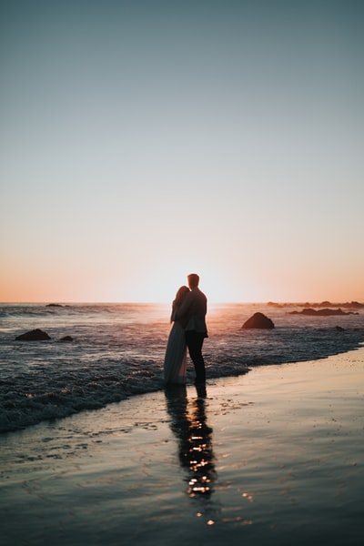 一对情侣站在海滩上观看日落的剪影照片